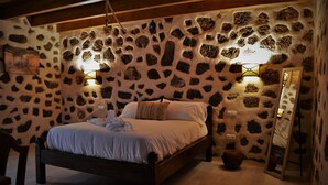 A bedroom with a stone wall, a wooden bed, two wall-mounted lights, and a mirror.
