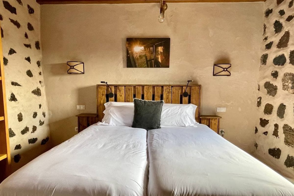 A double bed with white linens, a wooden headboard, and a single pillow.