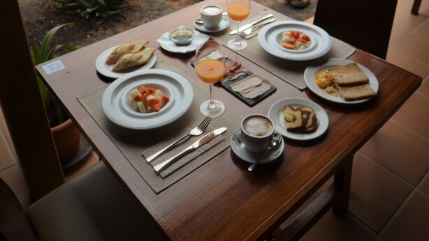 A dining table set with plates of food, a glass of juice, and a cup of coffee, overlooking a desert landscape with a mountain in the background.