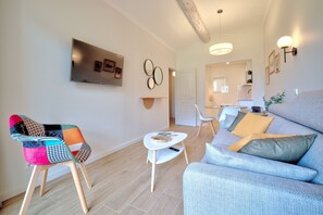 Un salon moderne avec un fauteuil coloré, un canapé gris et une petite table blanche.