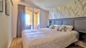 Ein Schlafzimmer mit einem großen Bett, einem Nachttisch, einem Sessel und Blick auf einen Balkon.