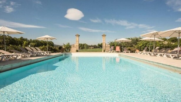 Ein klares Schwimmbecken mit Liegestühlen und Sonnenschirmen, umgeben von einer Umzäunung und Pflanzen.