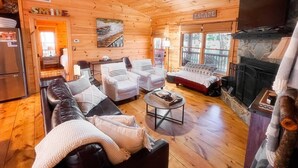 A cozy cabin interior with a fireplace, wooden walls, a ceiling fan, and a dining area. - Cozy lakeside cottage with outdoor haven for fishing, kayaking, and lounging (Ellijay)