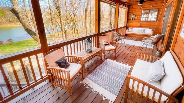A wooden deck with a view of a lake, furnished with chairs and a table. - Cozy lakeside cottage with outdoor haven for fishing, kayaking, and lounging (Ellijay)