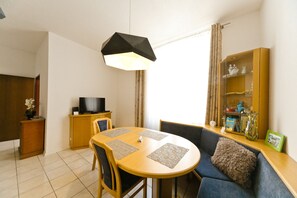 A compact living space with a round dining table, a sofa, a television on a wooden cabinet, and a bookshelf.