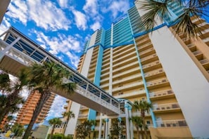 Un hotel moderno de gran altura con varios balcones, un puente peatonal y palmeras.