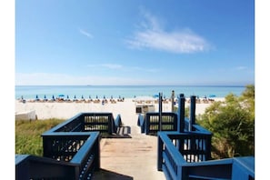 Un paseo marítimo de madera que conduce a una playa con sombrillas y sillas de descanso.
