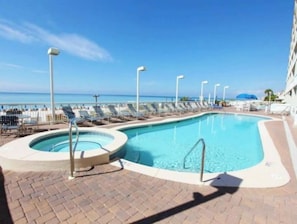 Zona de piscina con sillones de descanso y bañera de hidromasaje, con vista a una playa.