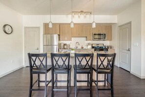 A modern kitchen with four black chairs, stainless steel appliances, and pendant lighting. - Luxury Suite King Bed Wi-Fi Pool Gym ✦ 55" Smart TVs Full Kitchen (Camarillo)