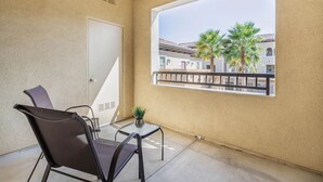 Un balcon avec vue sur des palmiers et un immeuble, une porte et une chaise.