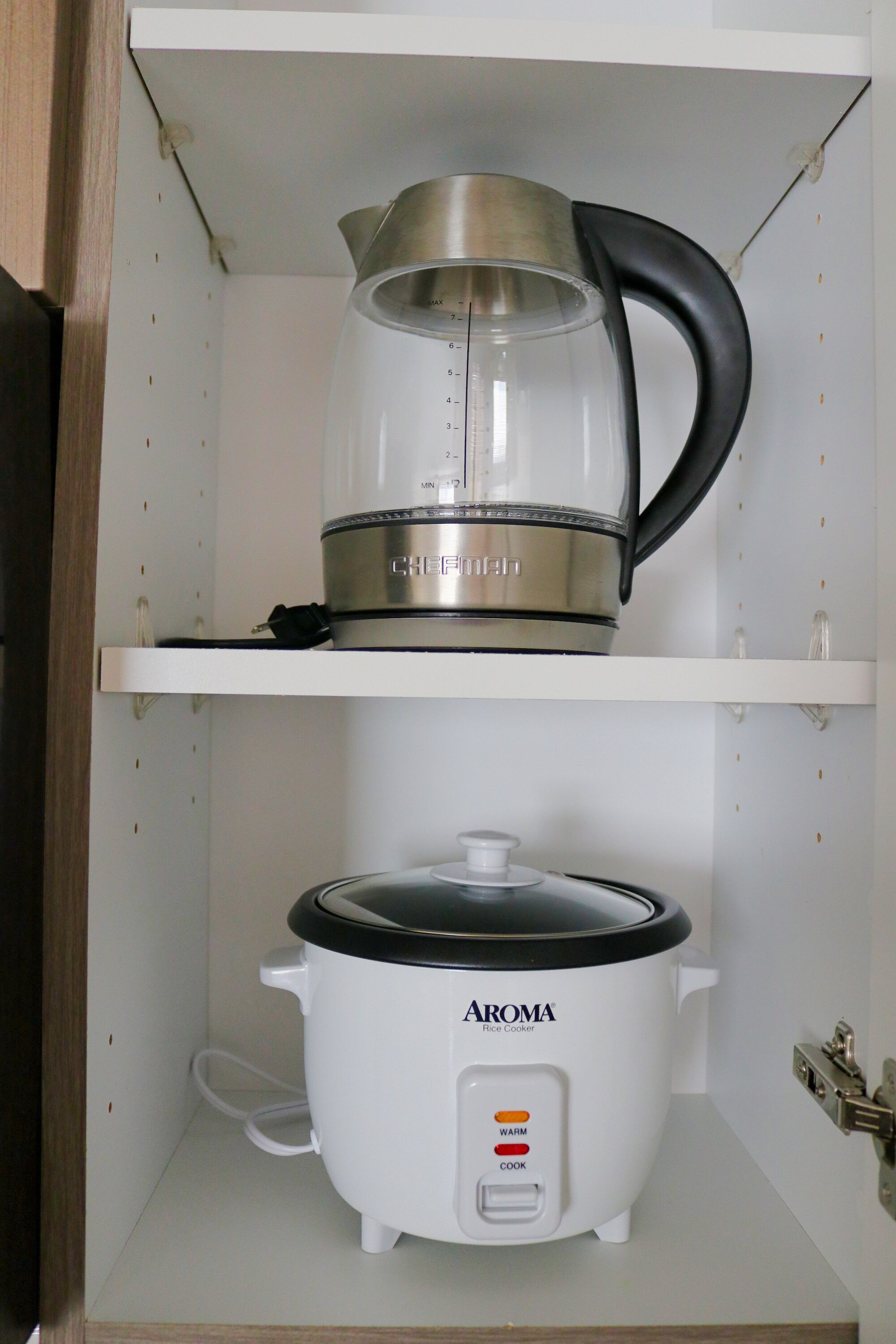 A kitchen with a CHEEFMAN coffee maker on the upper shelf and an AROMA rice cooker on the lower shelf.