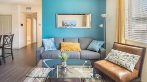 Un salon avec un mur d’accent bleu, un canapé gris agrémenté de coussins, une table basse en verre et un fauteuil en cuir marron.