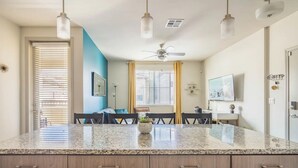 Une cuisine moderne dotée de plans de travail en granit, d’armoires en bois, d’un coin repas avec une table et des chaises, et d’un ventilateur de plafond.