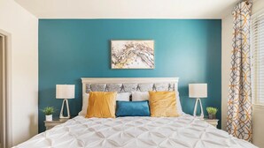 Une chambre avec un mur de couleur turquoise, une couvre-lit blanche et une tête de lit décorative.