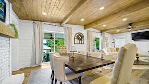 A spacious room with a wooden ceiling, a dining table with chairs, a sofa, and a TV mounted on the wall. - Canary Cottage Lakehouse on Jackson Lake (Mansfield)