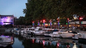 Un puerto deportivo con barcos amarrados, un escenario con luces y árboles decorados con iluminación.