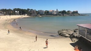Una playa con gente, cielo despejado y edificios al fondo.