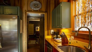 Una cocina con armarios de madera, un refrigerador de acero inoxidable, un lavamanos y una ventana decorada.