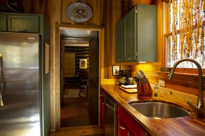 Una cocina con armarios de madera, un refrigerador de acero inoxidable, un lavamanos y una ventana decorada.