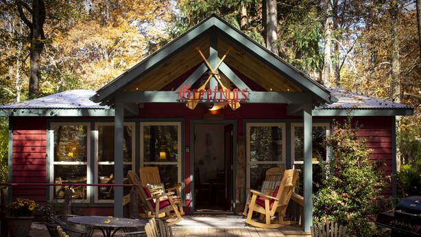 Eine Hütte mit Veranda, Holzstühlen und einem Tisch.