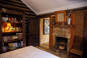 Une pièce chaleureuse avec une cheminée, des étagères en bois, un lit et un fauteuil.