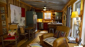 Ein gemütliches Blockhaus-Interieur mit einer Holzeinrichtung, einer Couch mit bunten Kissen und einer Küche mit Fenster und Deckenventilator.