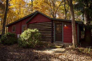 Una cabaña de troncos con fachada roja, una puerta principal y un porche pequeño.