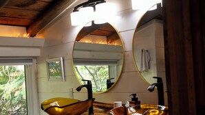 Ein Badezimmer mit einem Holzkosmetikschrank, einem großen, ovalen Spiegel und einem Waschbecken.