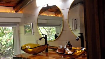 A bathroom with a wooden vanity, a large oval mirror, and a bowl sink.