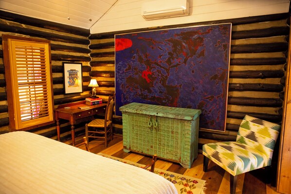 A log cabin room with a bed, desk, chair, and a large abstract painting on the wall.