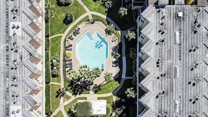 An aerial view of a hotel with a central pool surrounded by a landscaped area with palm trees and a hexagonal pool design. - Sassy Seahorse - FRONT ROW - Beach Views 8 Guests (Galveston)