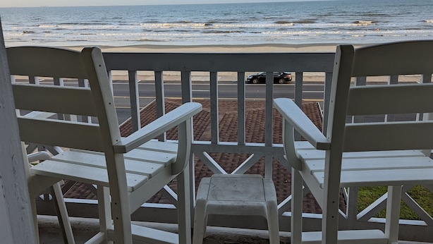 A beach view from a balcony with white chairs and a concrete floor. - Sassy Seahorse - FRONT ROW - Beach Views 8 Guests (Galveston)