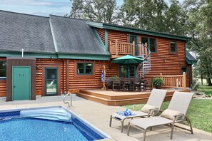 Una cabaña de troncos con piscina, mobiliario exterior y una escalera que lleva a una terraza.