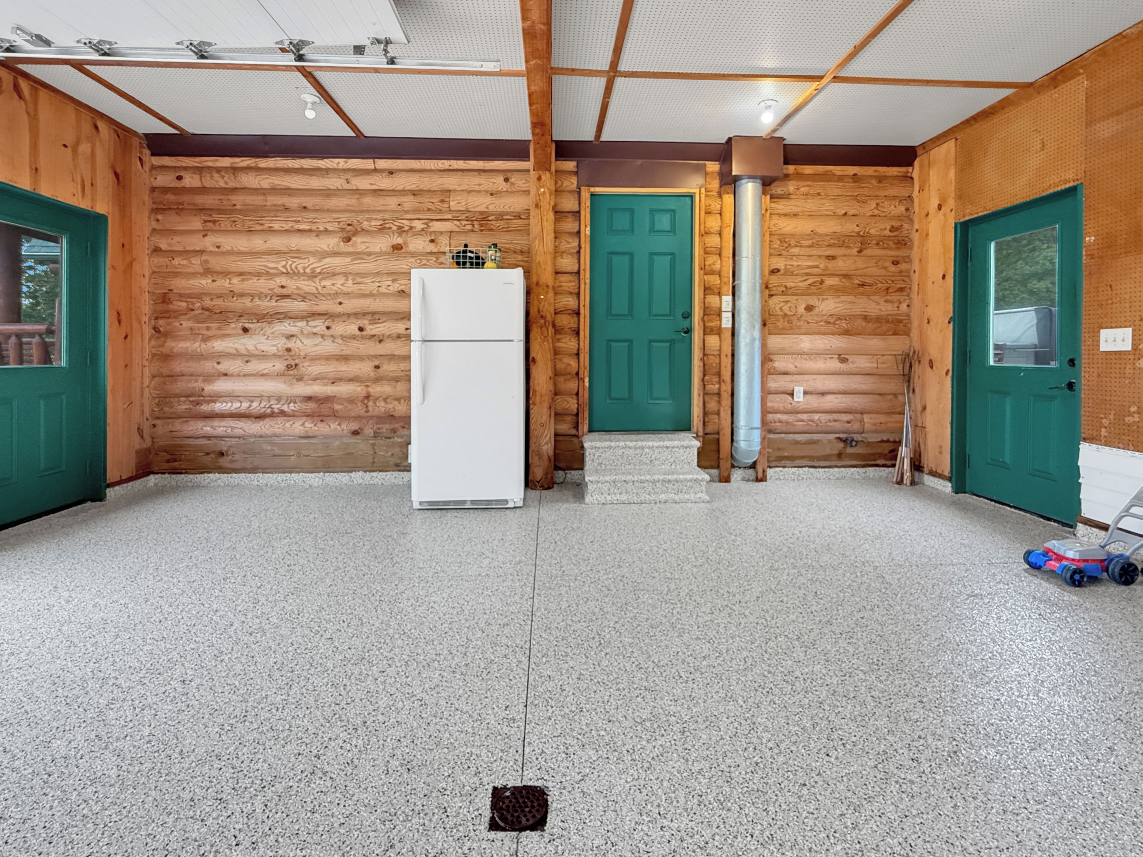 Het interieur van een blokhut met een witte koelkast, een groene deur en een betonnen vloer.