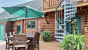 A wooden deck with a table and chairs, a green umbrella, and a potted plant. - Heated Seasonal Pool, Hot Tub & Theater • Rustic Cabin by Bike Path (Celina)