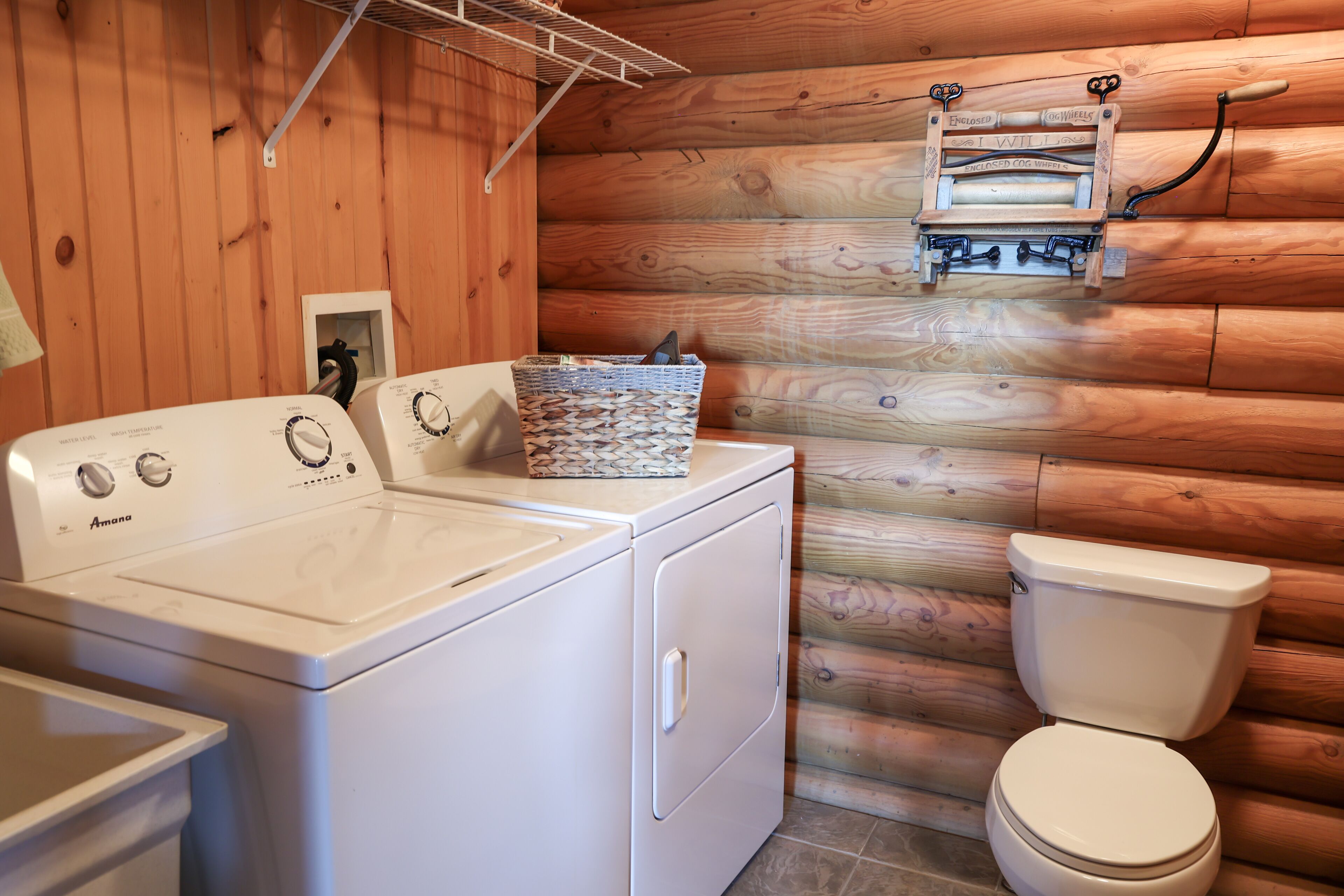 A compact laundry room with a front-loading washer and dryer, a wooden wall, and a white toilet.