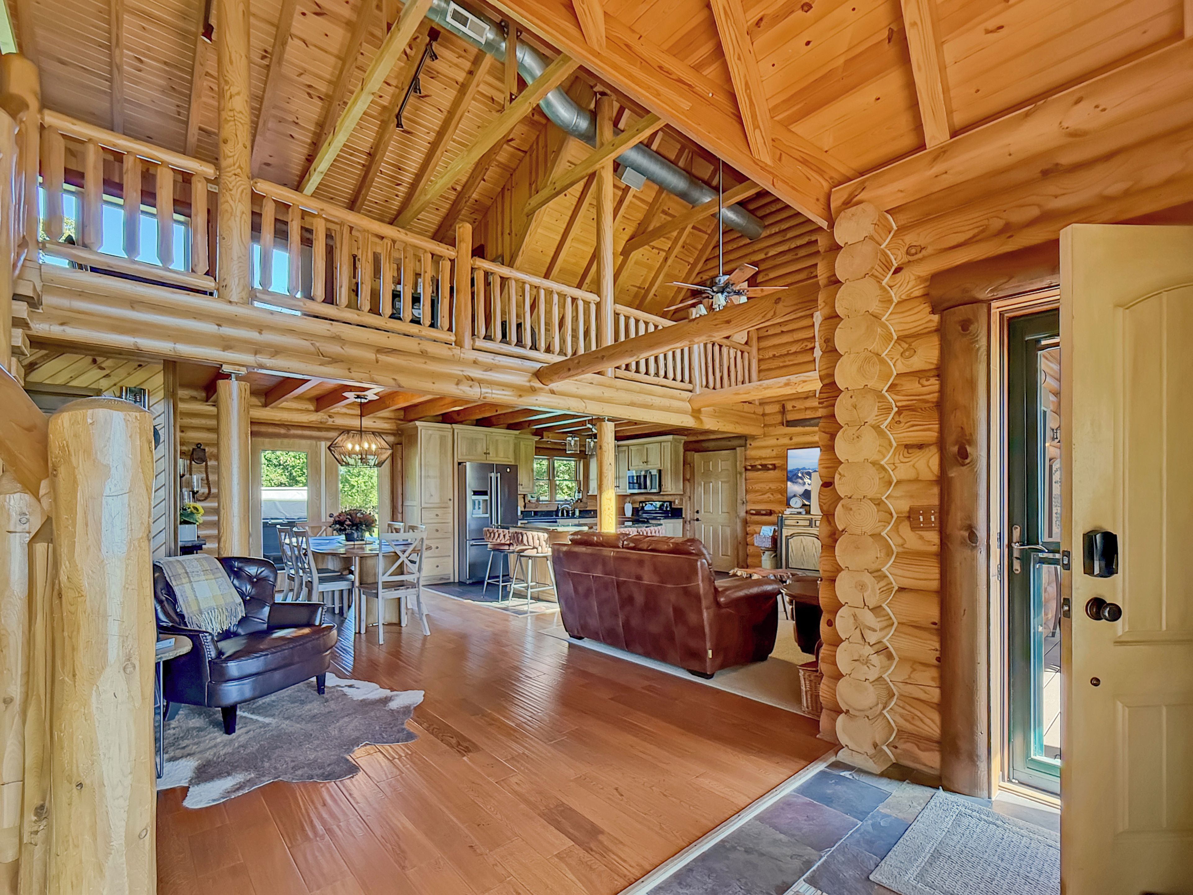 A spacious log cabin interior with a dining area, kitchen, and a loft bedroom.