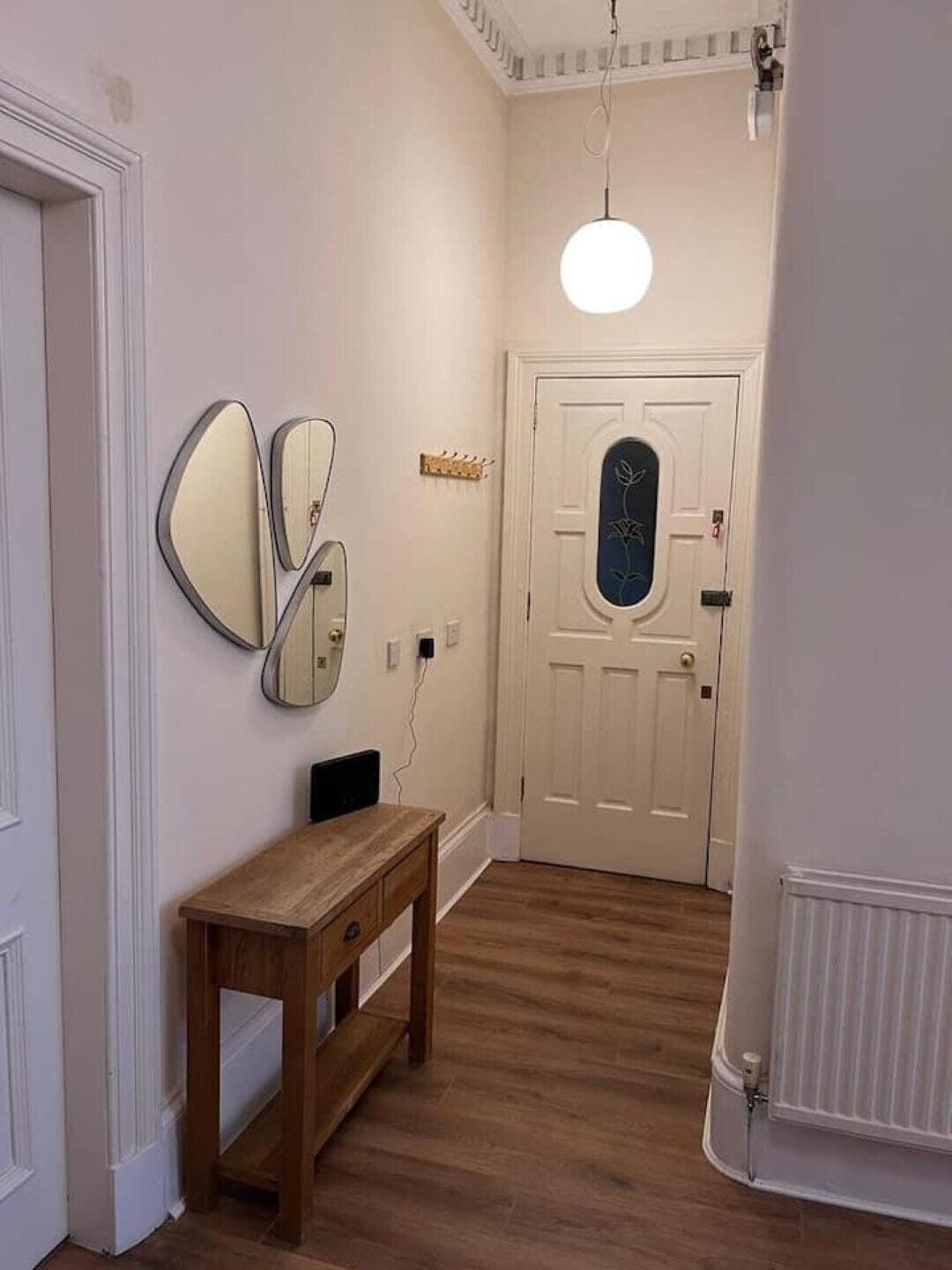 Um corredor com um banco de madeira, uma porta com painel de vidro decorativo e espelhos fixados na parede.