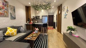 Een moderne woonkamer met een bank, salontafel en een televisie op een standaard. Er is een keukenhoek met een eettafel en stoelen.