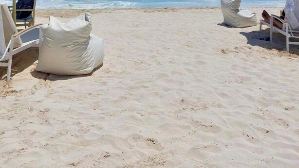 Une plage avec des chaises longues blanches et des parasols à rayures, un ciel bleu dégagé et des vagues océaniques calmes.
