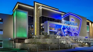 A modern building with a prominent "TOPGOLF" sign, large windows, and a well-lit entrance with stairs. - Modern Island Getaway with Heated pool added fee, Bar & Gazebo (Gilbert)
