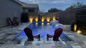 A swimming pool with two red chairs, a basketball hoop, and a brick wall. - Modern Island Getaway with Heated pool added fee, Bar & Gazebo (Gilbert)