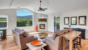 A modern living room with a fireplace, large windows, and a dining area. - Sedona Gecko Retreat: Luxurious 4BR home with red rock views and private pool. (Sedona)