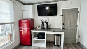 Une petite cuisine équipée avec un réfrigérateur rouge, un four à micro-ondes, une machine à café et une poubelle.