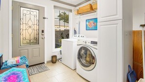 Un espace buanderie compact comprenant un lave-linge, une porte ornée d’un panneau de verre décoratif, une fenêtre et un petit tapis.