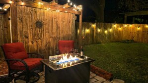 Une terrasse extérieure avec un foyer, deux chaises rouges et des guirlandes lumineuses.