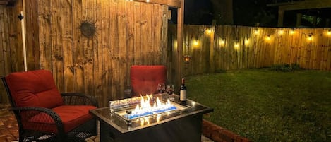 Une terrasse extérieure avec un foyer, deux chaises rouges et des guirlandes lumineuses.