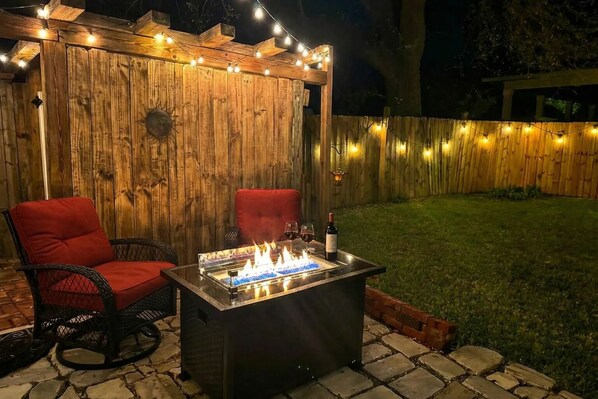 An outdoor patio with a fire feature, two red chairs, and string lights. - Quiet. Private. Perfect. Courtyard Suite for Two (Pensacola)