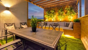 An outdoor patio with a wooden table and chairs, a cushioned sofa, and potted plants. - Luxury Midtown Houston Home w/ Rooftop Skyline Views (Houston)