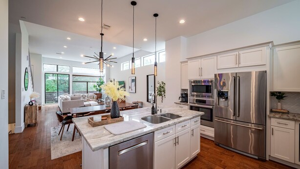 A modern kitchen with stainless steel appliances, a central island, and a dining area with a sofa and table. - Luxury Midtown Houston Home w/ Rooftop Skyline Views (Houston)